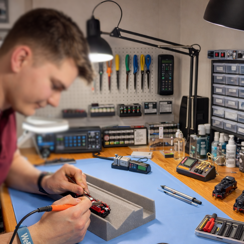 Modellbahn Werkstatt Junger Mann in einer Werkstatt für Modelleisenbahnen repariert eine Modellbahn.